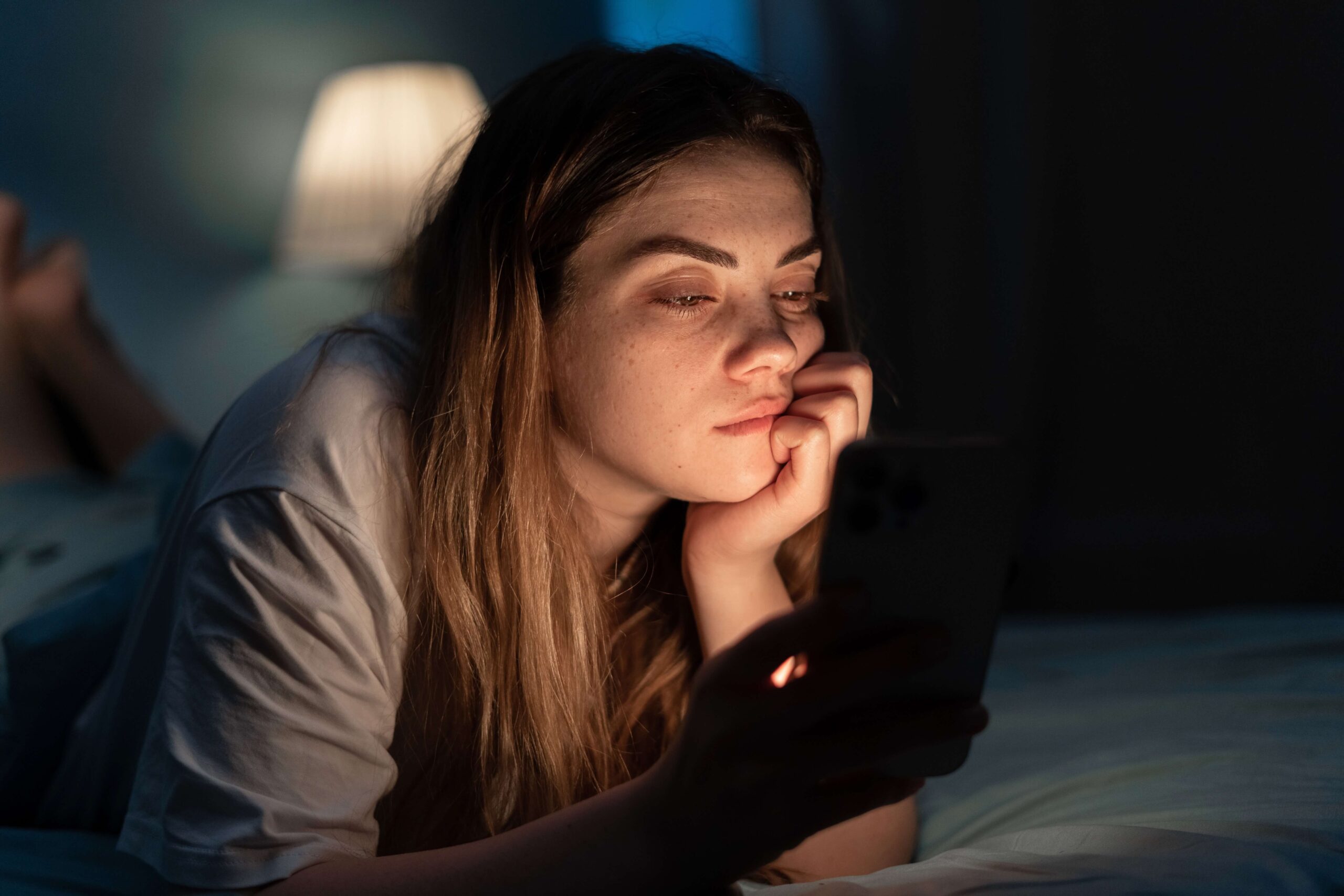 Young female checking her cell phone in the dark with pregnancy concerns—she is contemplating how to calculate her due date